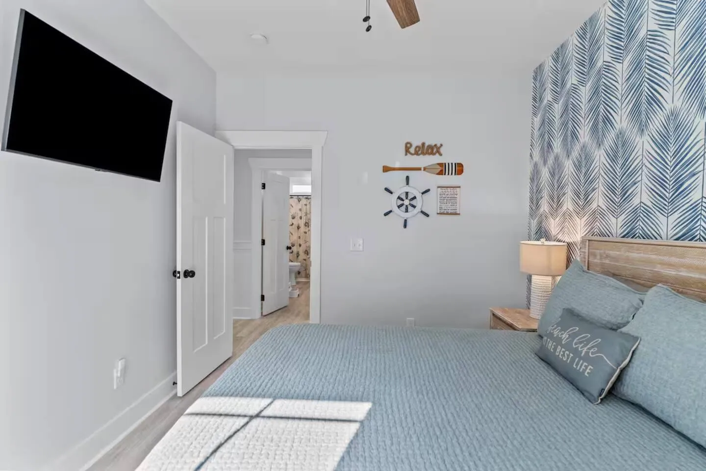 Queen bedroom with white bedding, a 'Relax' sign, and coastal wallpaper accent