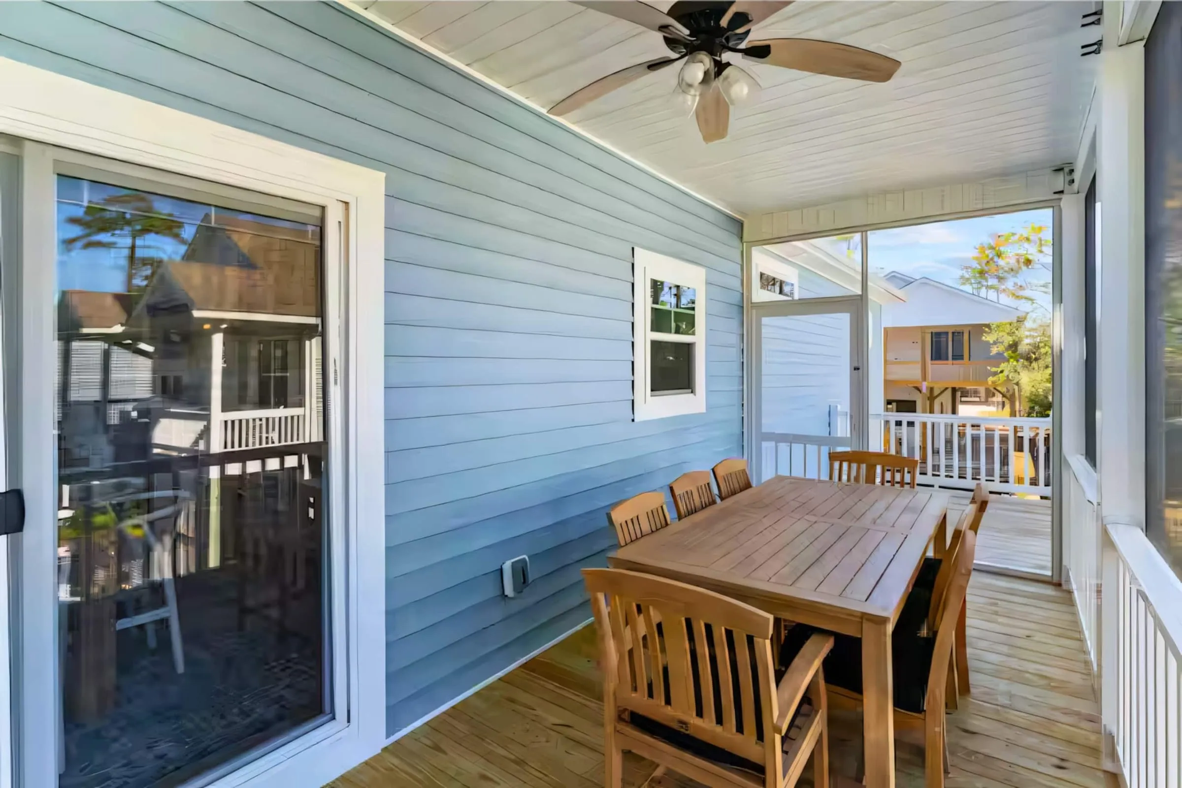Screened porch with a wooden dining table, ceiling fan, and a view of the yard